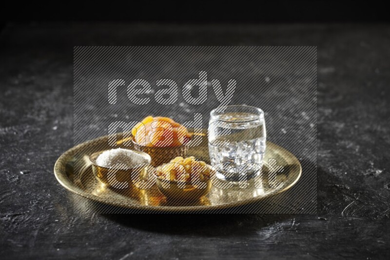 Dried fruits in metal bowls with water on a tray in dark setup