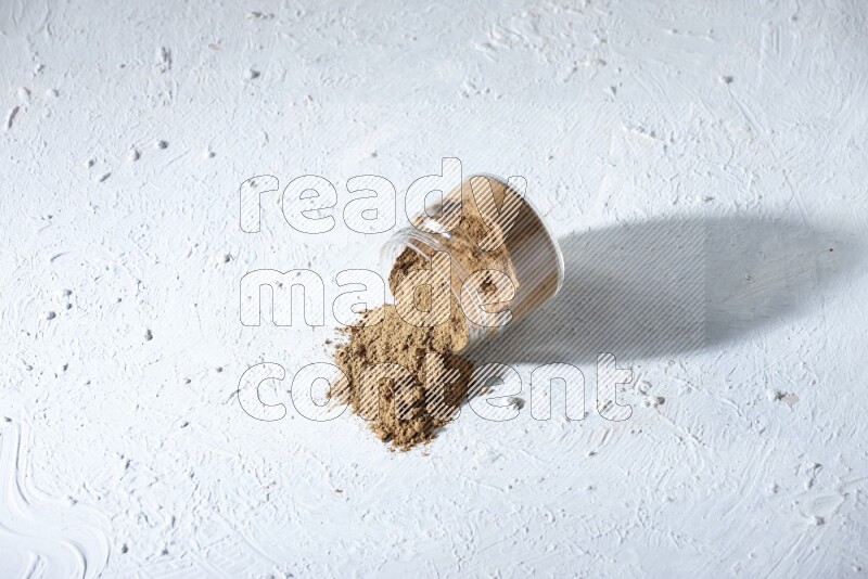 A flipped glass jar full of allspice powder and powder spilled out of it on a textured white flooring