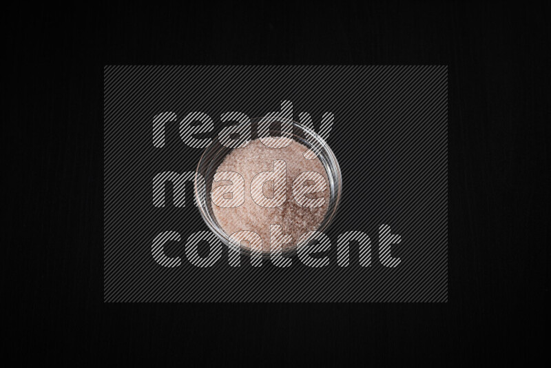 A glass bowl full of fine himalayan salt on black background