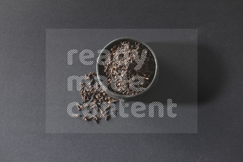 A black pottery bowl full of cloves on a black flooring