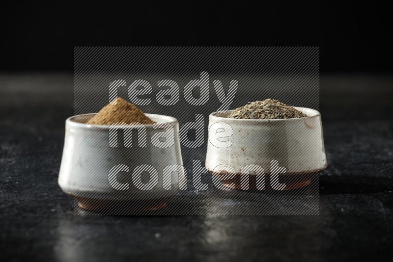 وعاءين بيج، أحدهما ممتلئ ببودرة الكمون والآخر ممتلئ بحبوب الكمون، على خلفية سوداء