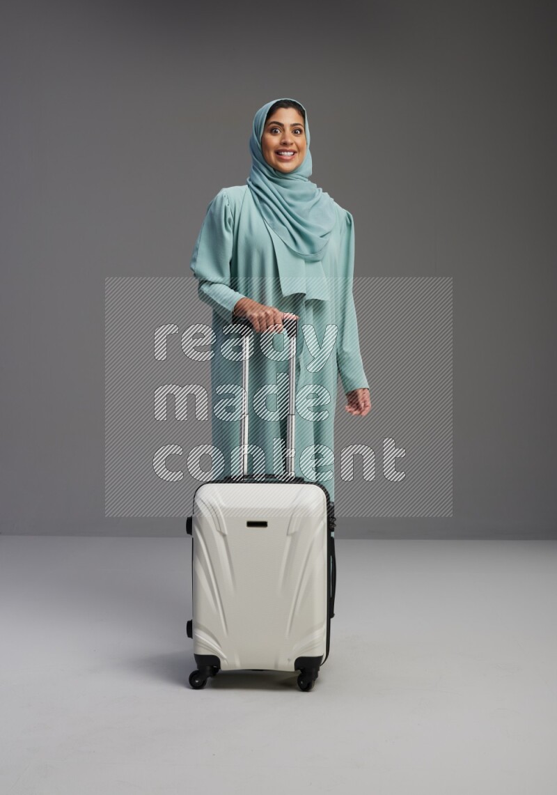 Saudi Woman wearing Abaya standing holding Travel bag on Gray background