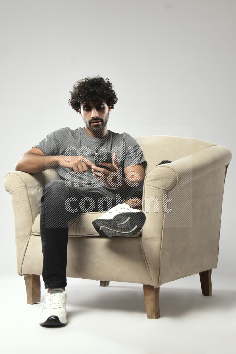 A man wearing casual sitting on a chair browsing on the phone on white background