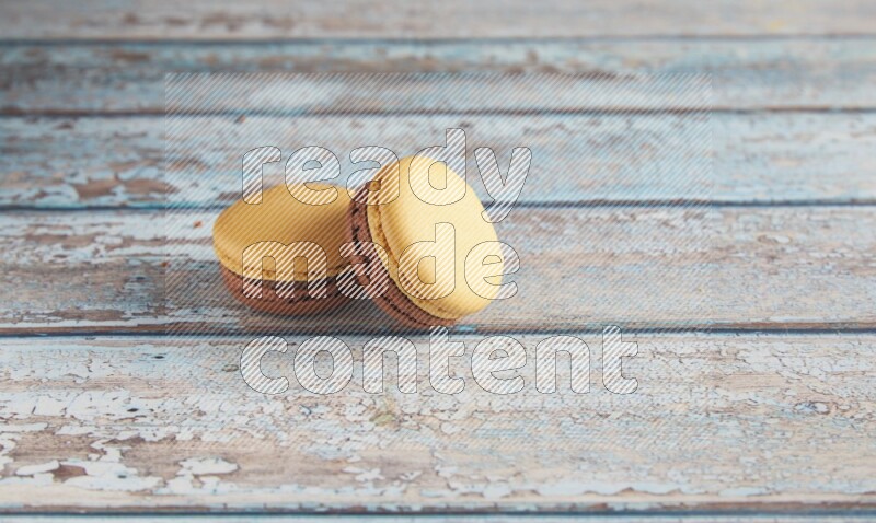 45º Shot of two Yellow and Brown Chai Latte macarons on light blue wooden background