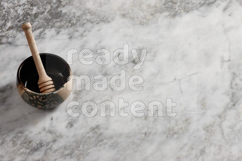 وعاء فخاري متعدد الألوان مع ملعقة عسل خشبية بداخله على خلفية من الرخام الرمادي