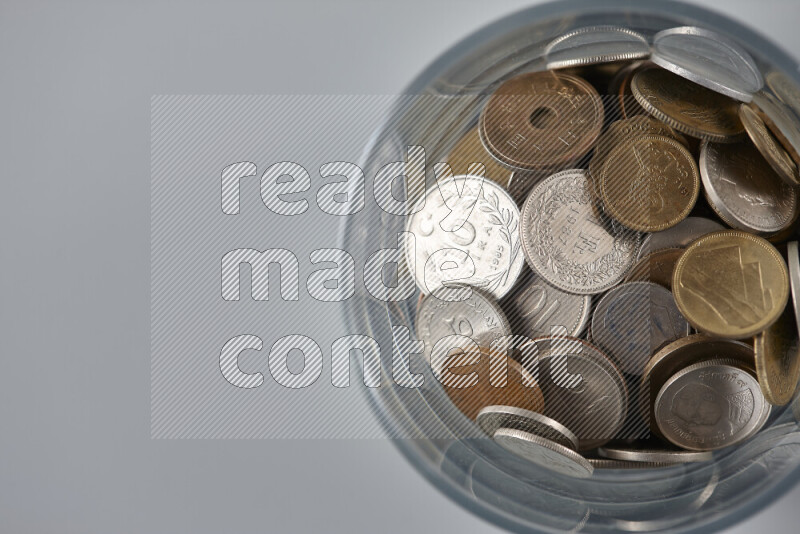 Random old coins in a glass cup on grey background