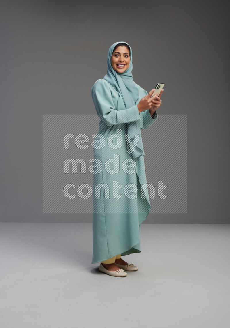 Saudi Woman wearing Abaya standing texting on phone on Gray background