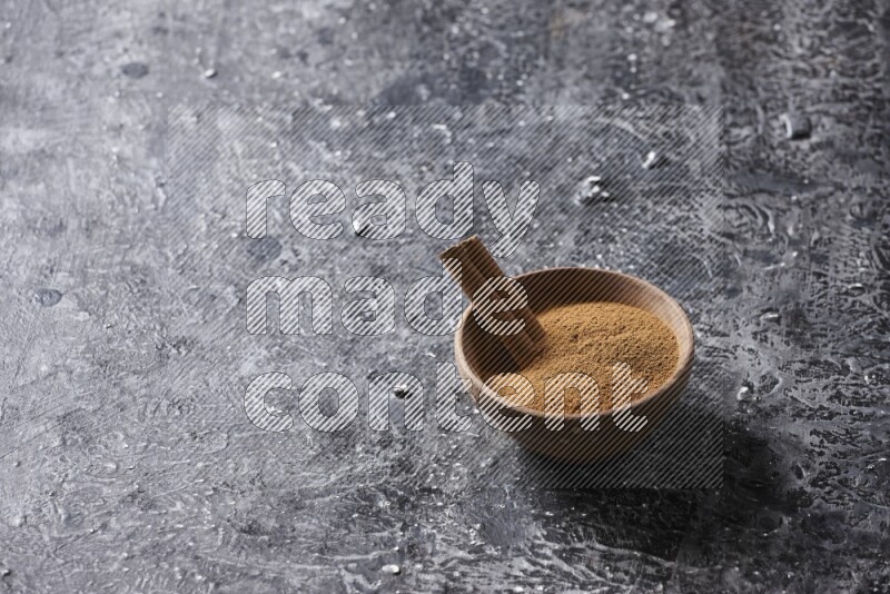 Wooden bowl full of cinnamon powder and a cinnamon stick on a textured black background