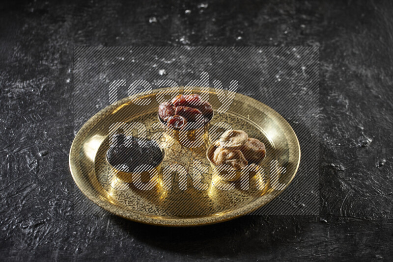 Dried fruits in metal bowls on a tray in a dark setup