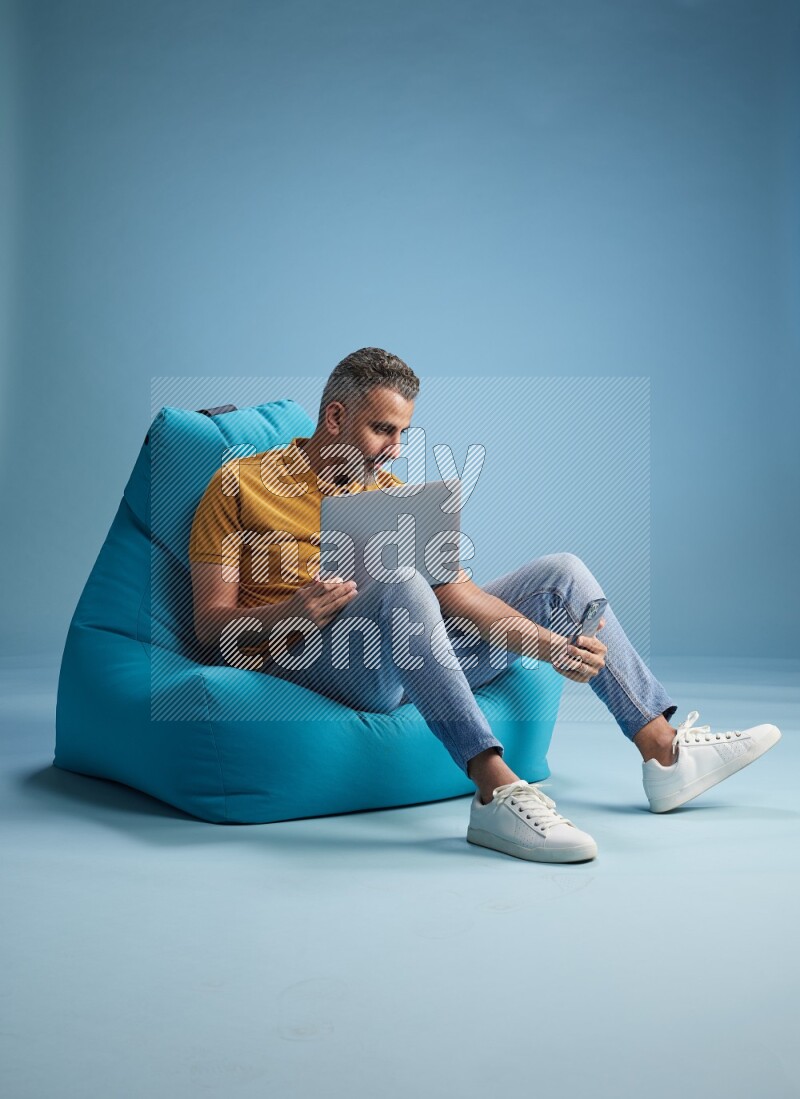 A man sitting on a blue beanbag and working on laptop
