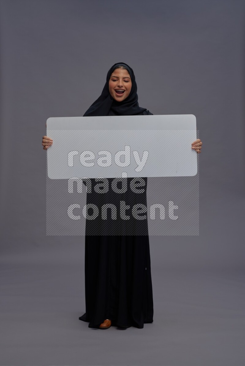 Saudi woman wearing Abaya standing holding white board on gray background