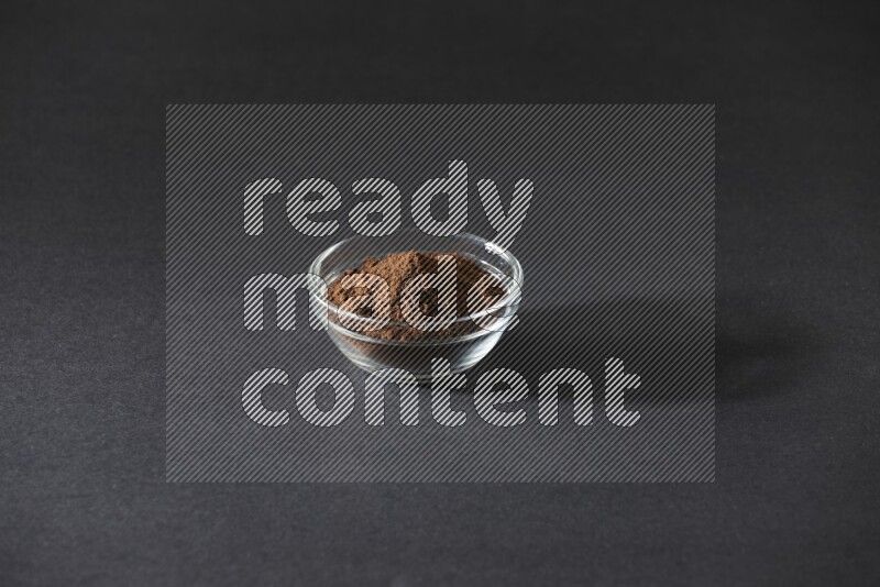 A glass bowl full of cloves powder on black flooring
