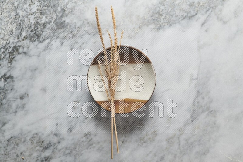 Wheat stalks on multicolored pottery plate on grey marble background
