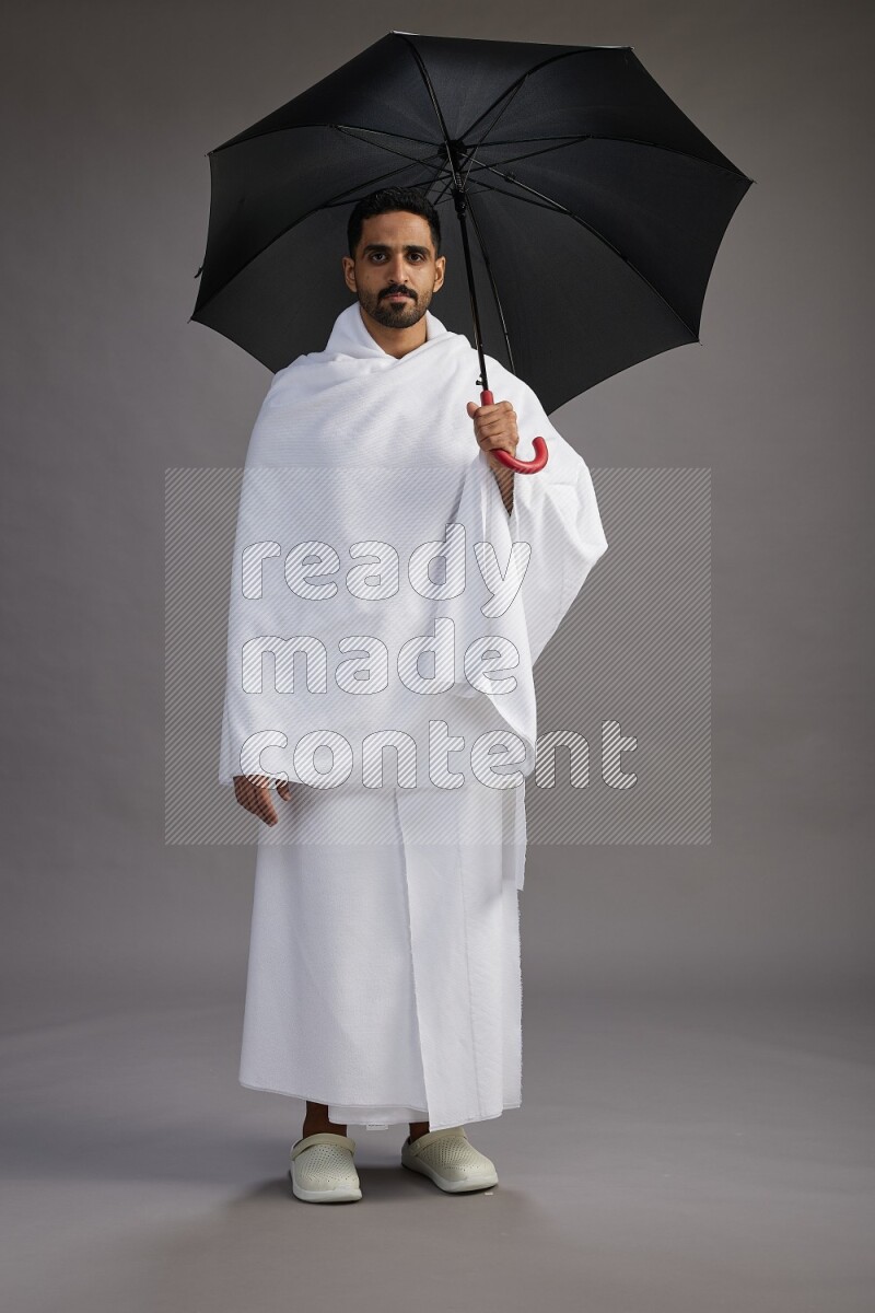 A man wearing Ehram Standing holding umbrella on gray background