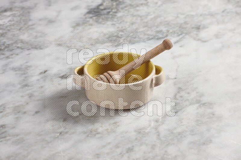Multicolored pottery bowl with wooden honey dipper in it on grey marble background