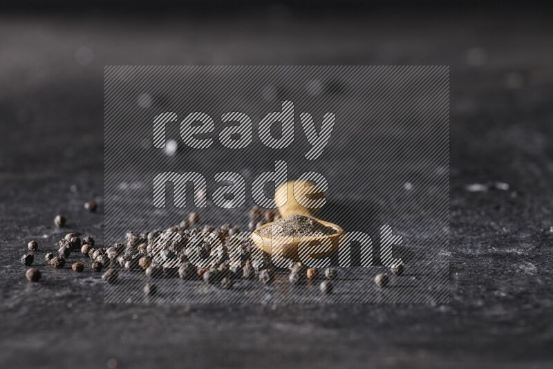 حبوب الفلفل الأسود في ملعقة خشبية مع حبوب الفلفل منتشرة علي خلفية سوداء