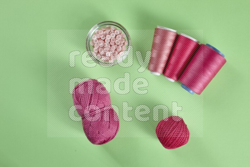 A pink collection of sewing and tailoring tools arranged on a green background