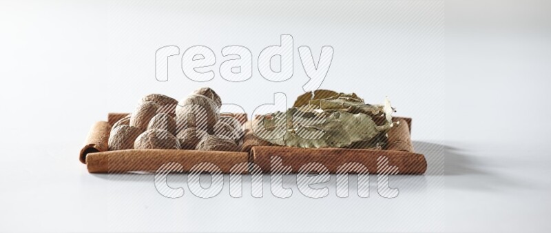 مربعان من أعواد القرفة ممتلئان بأوراق الغار وجوزة الطيب علي خلفية بيضاء