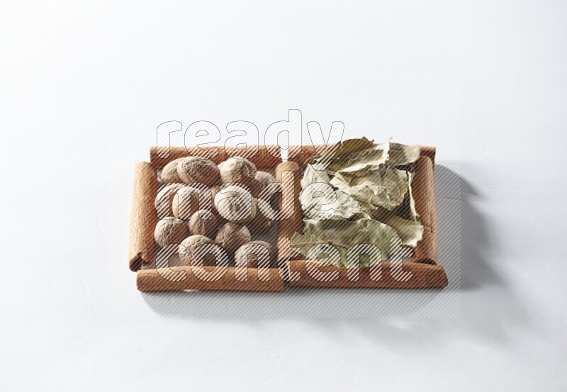 مربعان من أعواد القرفة ممتلئان بأوراق الغار وجوزة الطيب علي خلفية بيضاء