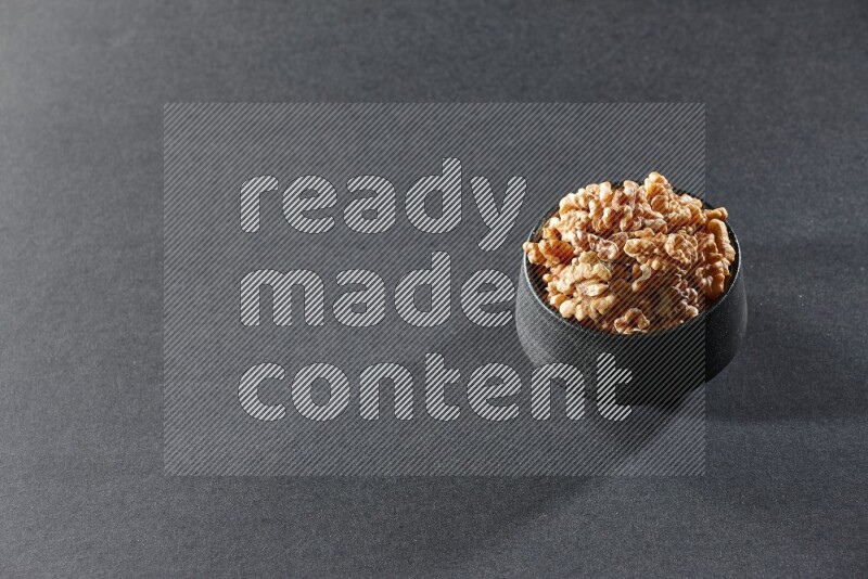A black pottery bowl full of peeled walnuts on a black background in different angles
