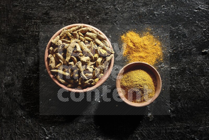 وعاءان خشبيان، أحدهما ممتلئ ببودرة الكركم والآخر بأصابع الكركم المجففة، على خلفية سوداء