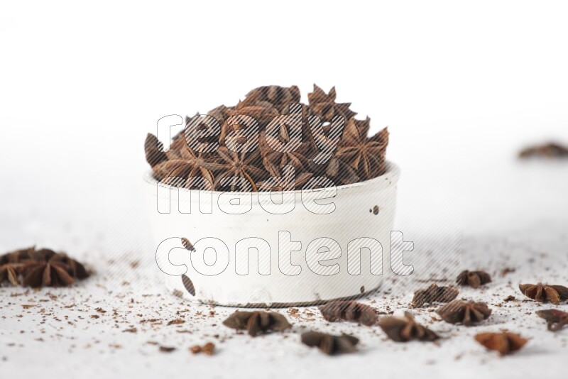 Star Anise in a white bowl and more of it sprinkled on white background