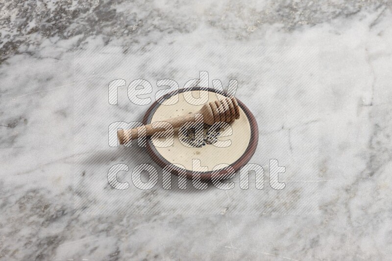 Decorative pottery plate with wooden honey dipper in it on grey marble background