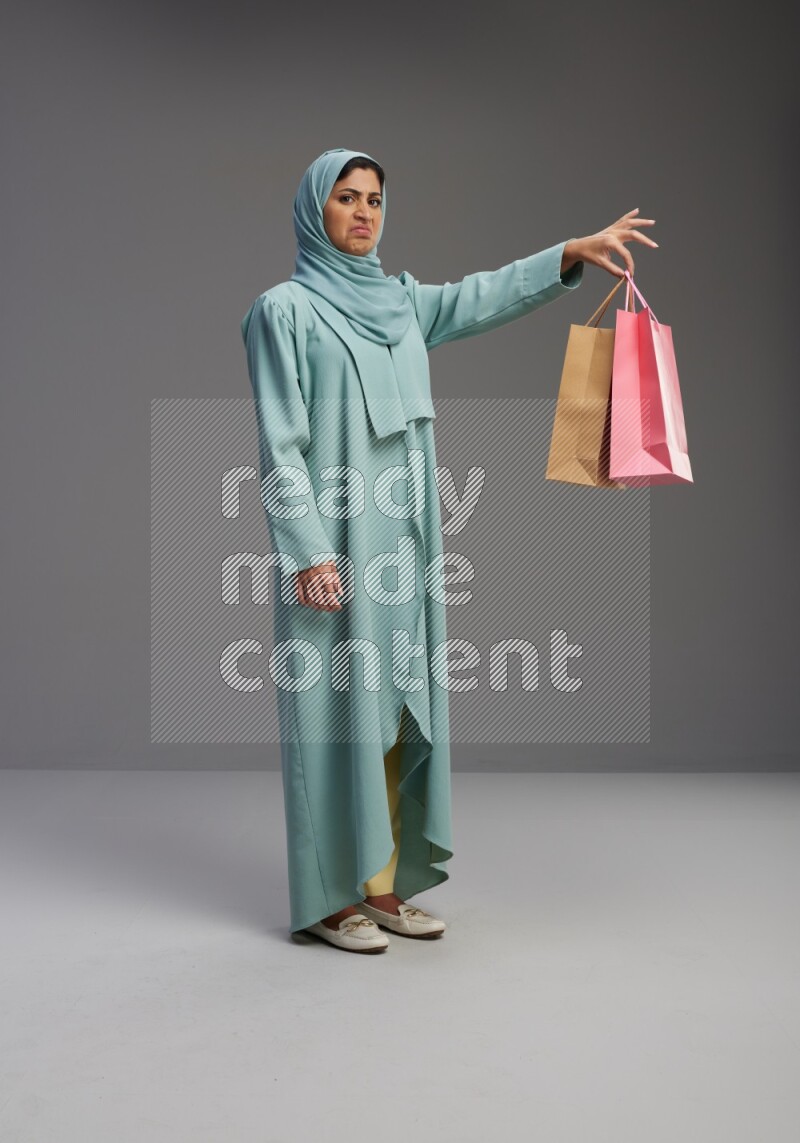 Saudi Woman wearing Abaya standing holding shopping bag on Gray background