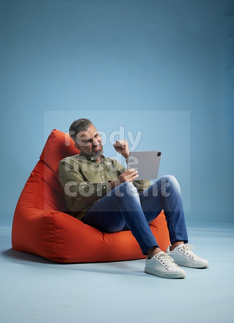 A man sitting on an orange beanbag and working on tablet