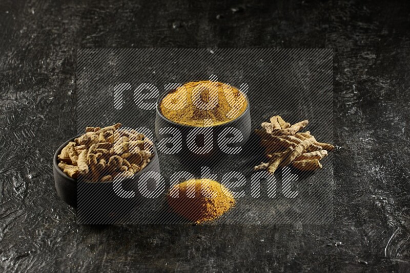 وعاءان من الفخار باللون الأسود، أحدهما ممتلئ ببودرة الكركم والآخر ممتلئ بأصابع كاملة من الكركم المجفف على خلفية سوداء