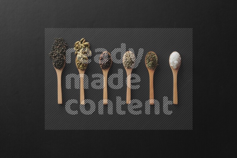 wooden spoons filled with white peppers, cloves, cardamom, salt, black peppers and basil on black flooring
