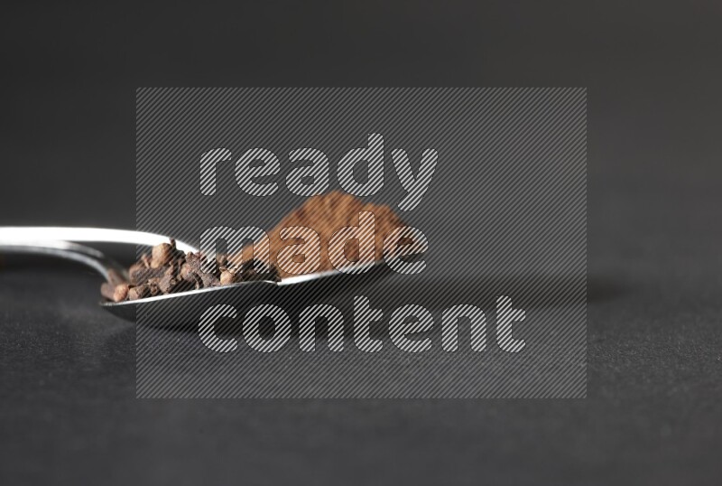 ملعقتان معدنيتان، إحداهما ممتلئة بحبوب القرنفل والأخرى ببودرة القرنفل، على خلفية سوداء