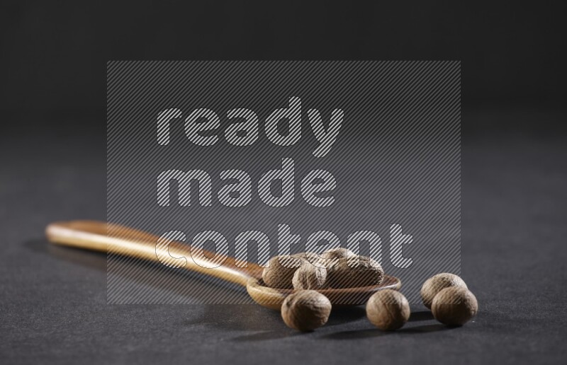 ملعقة خشبية كبيرة مليئة بحبوب جوزة الطيب الكاملة على خلفية سوداء