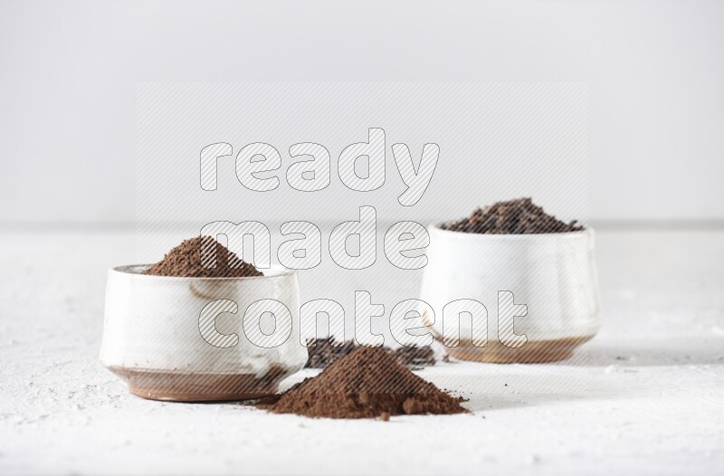 2 Beige ceramic bowls, one full of cloves and the other full of powder on textured white flooring