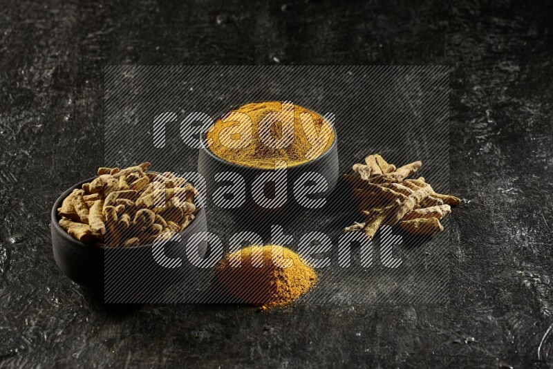 وعاءان من الفخار باللون الأسود، أحدهما ممتلئ ببودرة الكركم والآخر ممتلئ بأصابع كاملة من الكركم المجفف على خلفية سوداء