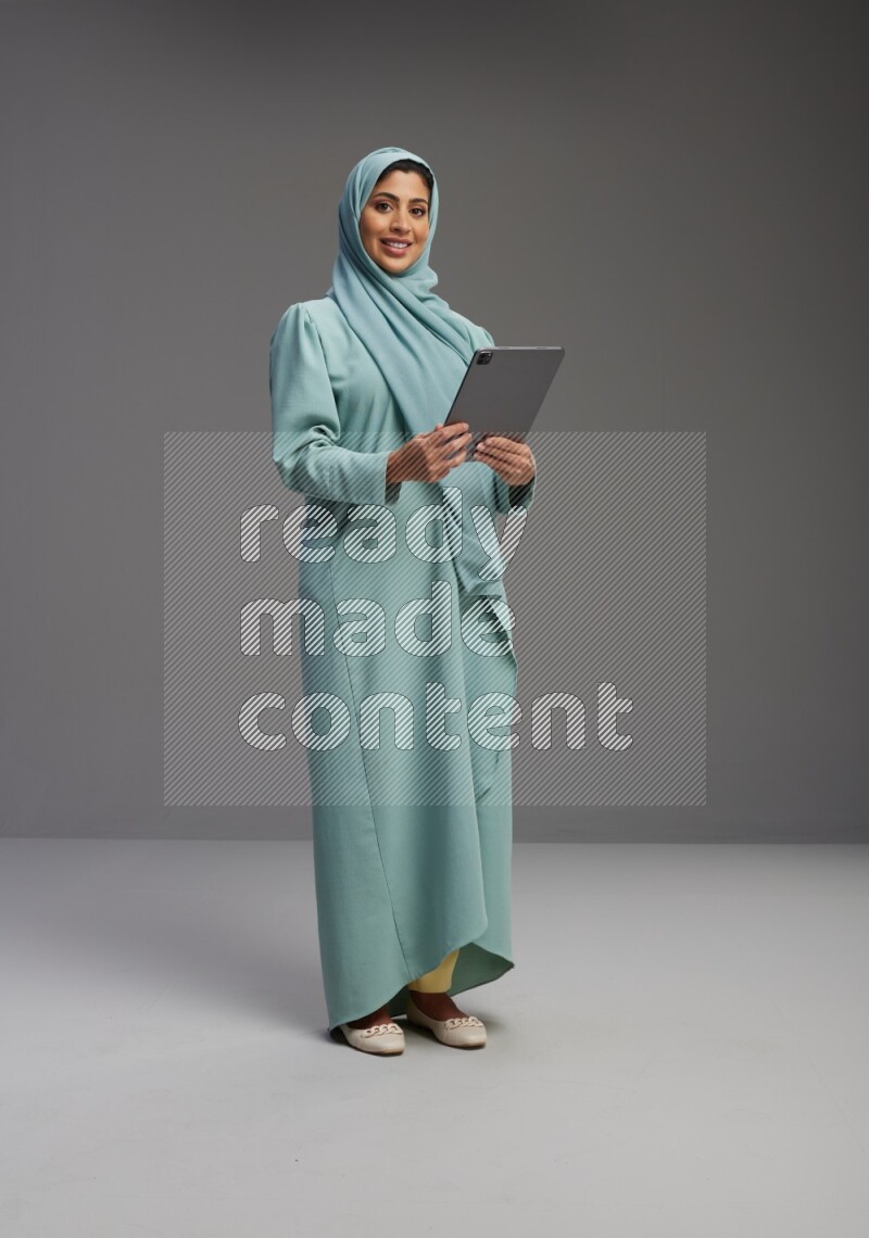 Saudi Woman wearing Abaya standing working on tablet on Gray background