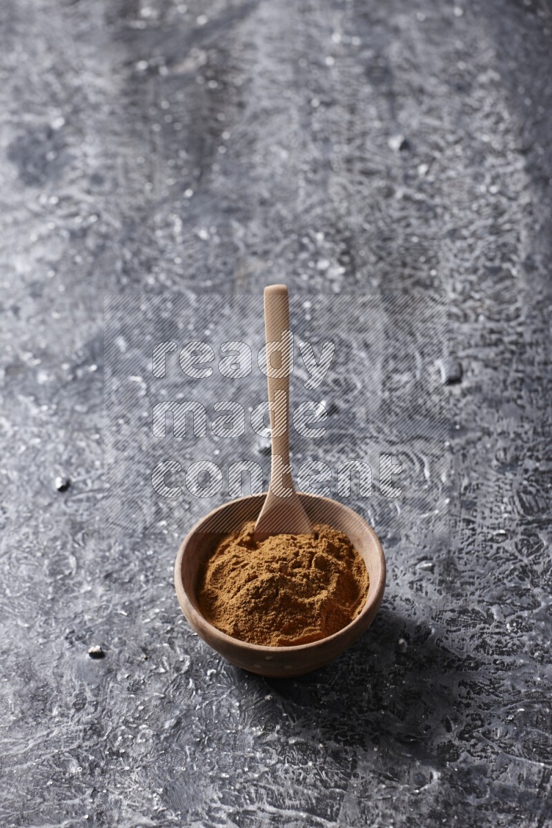 Wooden bowl full of cinnamon powder with a wooden spoon on a textured black background in different angles