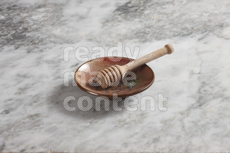 Decorative pottery plate with wooden honey dipper in it on grey marble background