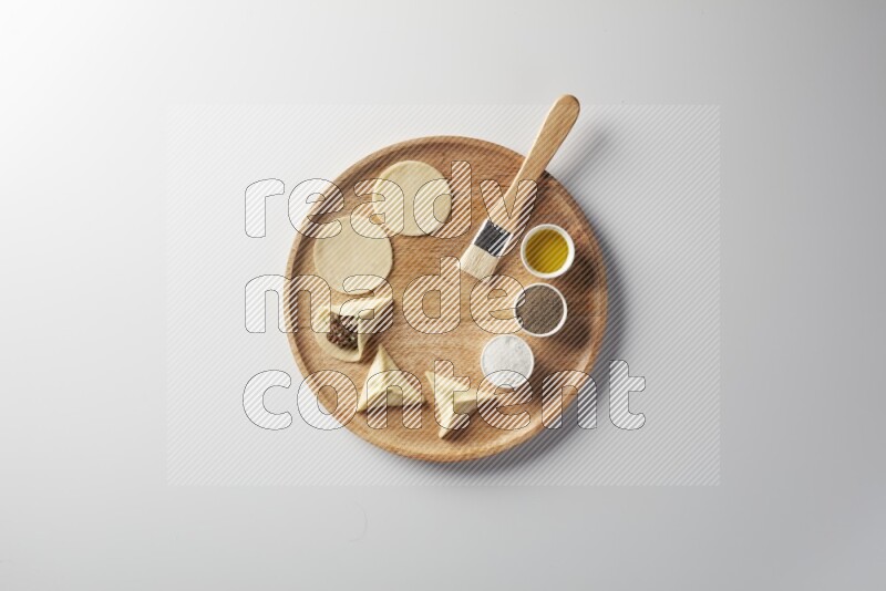 two closed sambosas and one open sambosa filled with meat while salt, black pepper and oil with oil brush aside in a wooden dish on a white background