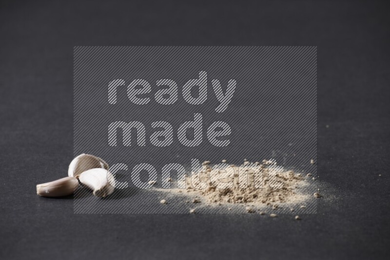 A small pile of garlic powder with some of cloves and a whole garlic bulb on a black flooring