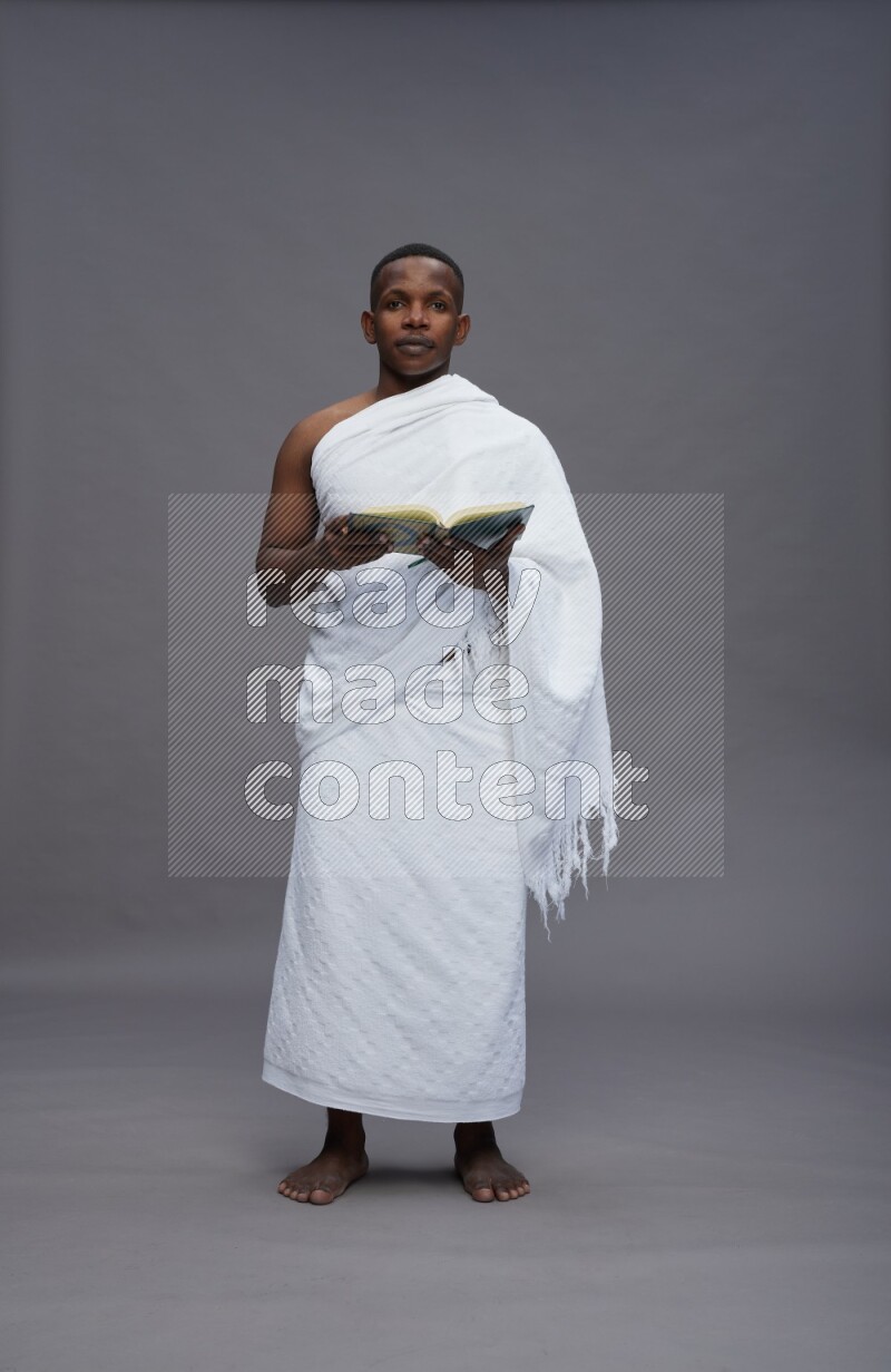 A man wearing Ehram Standing reading quran on gray background