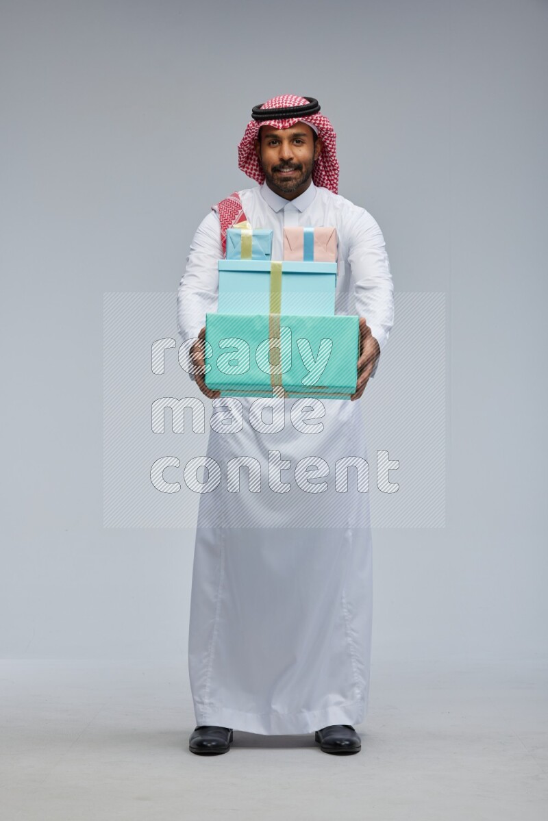 Saudi man Wearing Thob and shomag standing holding gift box on Gray background