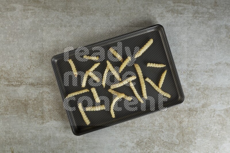 crinkle fries in a black stainless steel rectangle tray on grey textured counter top