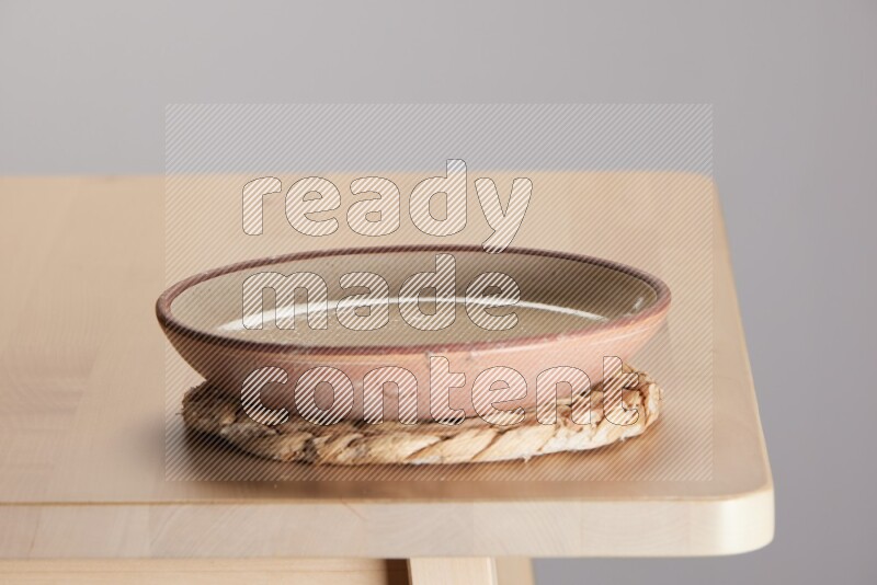 multi-colored pottery Plate placed on a small light colored straw placemat on the edge of wooden table