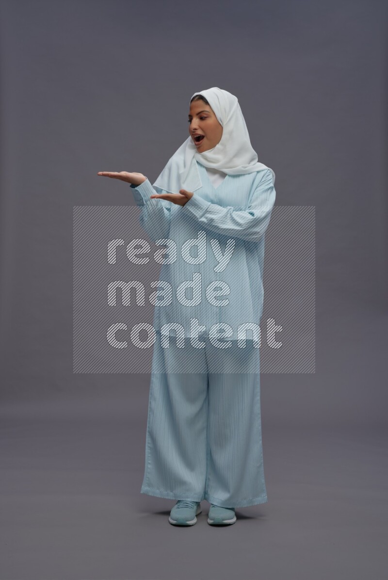 Saudi woman wearing hijab clothes standing interacting with the camera on gray background