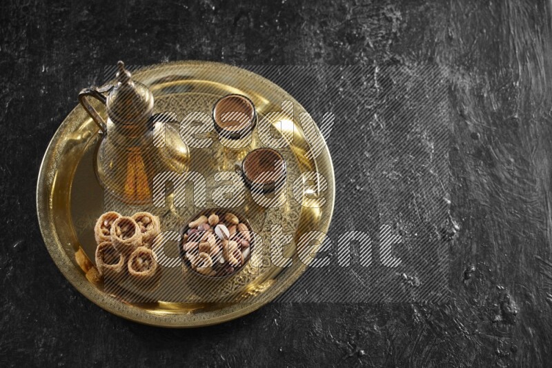 Oriental sweets with nuts and a drink on a metal tray in a dark setup