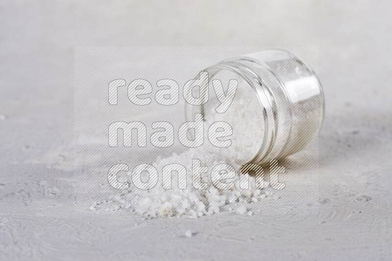 A glass jar full of coarse sea salt crystals on white background