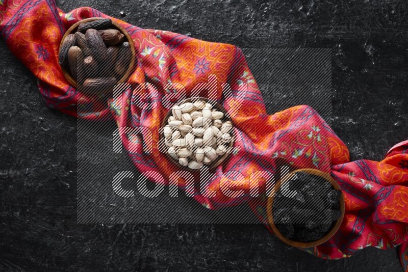 Dried fruits and nuts in wooden bowls in a dark setup