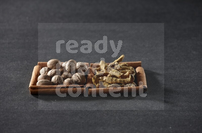 مربعان من أعواد القرفة ممتلئان بجوزة الطيب وأصابع الكركم علي خلفية سوداء