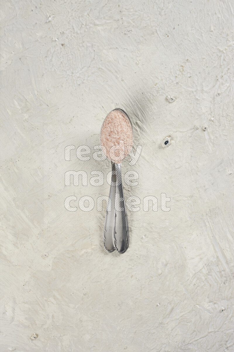 2 metal spoons filled with fine table salt and fine pink himalayan salt on white background